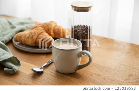 Cup of coffee with milk and fresh croissants  on a wooden table with napkin and coffee beans 125039558