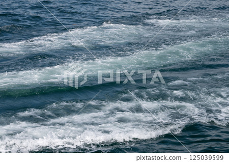 Ocean waves forming white foam trail on deep blue sea surface during daytime. Ocean waves forming white foam trail on deep blue sea surface during daytime. 125039599