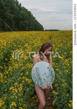 Artistic Woman Holding Mirror in Flower Field 125039932