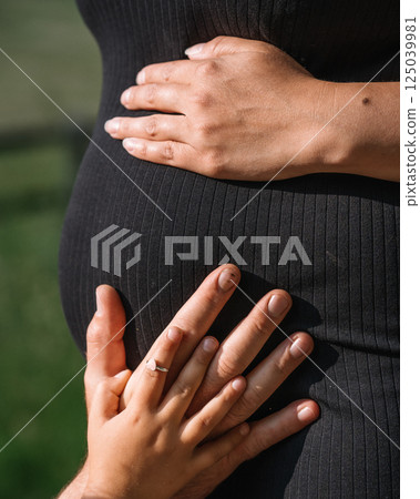 pregnant woman's belly in black dress close-up with mom and dad and daughter's hands on mom's belly. High quality photo pregnant woman's belly in black dress close-up with mom and dad and daughter's hands on mom's belly. High quality photo 125039981