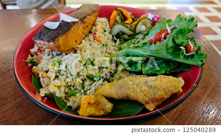 Delicious Fried Rice with Crispy Fried Salmon and Fresh Salad on Red Plate, Captured on Wooden Table in Cozy Restaurant Delicious Fried Rice with Crispy Fried Salmon and Fresh Salad on Red Plate, Captured on Wooden Table in Cozy Restaurant 125040289