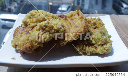 Crispy fried banana fritters on a white plate, golden brown and crunchy, photographed on a rustic wooden table, perfect for tropical dessert or snack imagery Crispy fried banana fritters on a white plate, golden brown and crunchy, photographed on a rustic wooden table, perfect for tropical dessert or snack imagery 125040334
