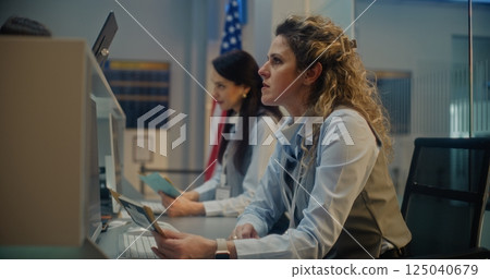 Female Airline Agents Checking Documents and Airplane Tickets of Passengers, Working on Computers 125040679