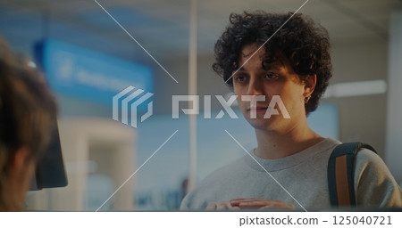 Airport Check-in Counter: Young Man Confirms Identity by Facial Recognition Scan 125040721