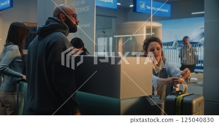 Airport Counter: Female Airline Check-in Attendant Checking Baggage, Putting Barcode Label on Suitcase Airport Counter: Female Airline Check-in Attendant Checking Baggage, Putting Barcode Label on Suitcase 125040830