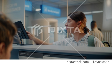 Female Airline Worker Checking Personal Data on Computer, Giving Documents and Boarding Pass to Woman 125040886