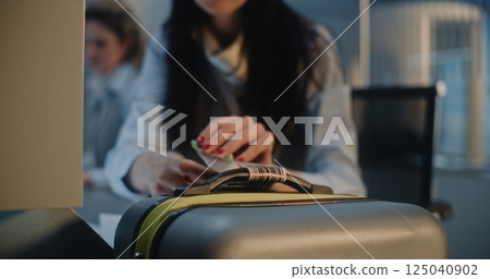 Female Airline Check-in Attendant Putting Baggage Tag Barcode on Suitcase for Boarding Flight 125040902