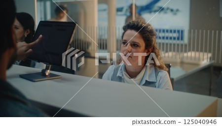 Airport Check-in Counter: Female Airline Agent Checking Traveler Biometric Data for Boarding Flight Airport Check-in Counter: Female Airline Agent Checking Traveler Biometric Data for Boarding Flight 125040946