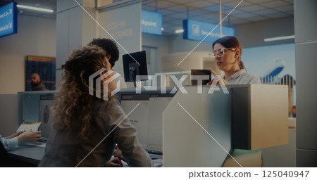 Airport Check-in Counter: Female Airline Worker Giving Documents and Boarding Pass to Woman Airport Check-in Counter: Female Airline Worker Giving Documents and Boarding Pass to Woman 125040947