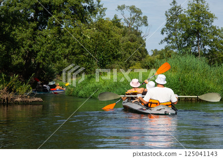 Family with children on rafting trip in Group kayak trip of different ages, adults, elderly. Rowing boat on the river, a water hike, summer adventure. 125041143