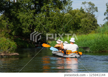 Family with children on rafting trip in Group kayak trip of different ages, adults, elderly. Rowing boat on the river, a water hike, summer adventure. 125041144