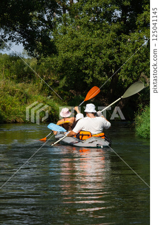Family with children on rafting trip in Group kayak trip of different ages, adults, elderly. Rowing boat on the river, a water hike, summer adventure. 125041145