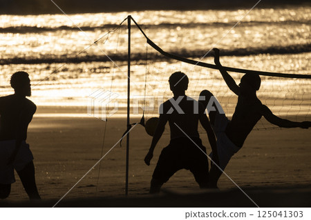 Athletes playing beach volleyball at sunset on tropical beach 125041303