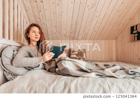 Woman Reading Book in Bed at Log Cabin Woman Reading Book in Bed at Log Cabin 125041364