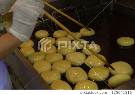 A chef skillfully frying golden dough balls in hot oil, creating a delicious culinary delight. 125041516