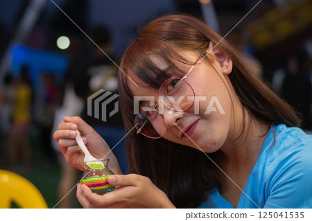 A young woman enjoys a colorful dessert, showcasing a playful and cheerful atmosphere with friends around her. A young woman enjoys a colorful dessert, showcasing a playful and cheerful atmosphere with friends around her. 125041535