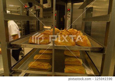 Freshly baked pastries cooling on a rack in a professional kitchen, showcasing delicious textures and colors. Freshly baked pastries cooling on a rack in a professional kitchen, showcasing delicious textures and colors. 125041590