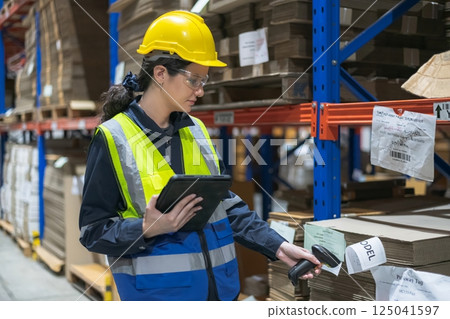 A worker scanning inventory in a warehouse using a tablet and barcode scanner, showcasing modern logistics. 125041597