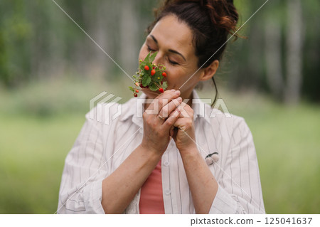 Female with closed eyes smelling wild berries in forest enjoying relaxation and calmness. Female enjoying healthy lifestyle, eco living and nature retreat outdoors Female with closed eyes smelling wild berries in forest enjoying relaxation and calmness. Female enjoying healthy lifestyle, eco living and nature retreat outdoors 125041637