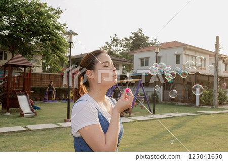 A woman blowing bubbles in a sunny park, enjoying a playful moment in a vibrant outdoor space. 125041650