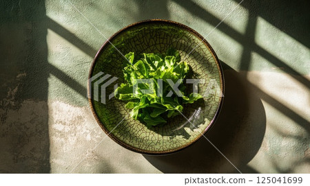 Minimalist still life of leafy greens with sunlight shadows in a serene indoor setting 125041699