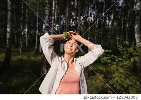 Adult woman enjoying nature moment in forest with wild strawberry bouquet. Female relaxing outdoors feeling harmony, freedom and positive emotions 125042008