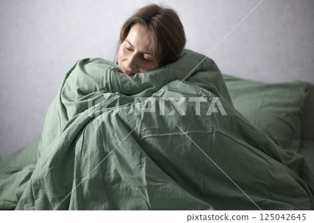woman sitting in bed wrapped in a blanket woman sitting in bed wrapped in a blanket 125042645