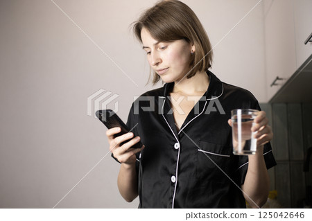 woman holding a glass of water and looking at her phone woman holding a glass of water and looking at her phone 125042646