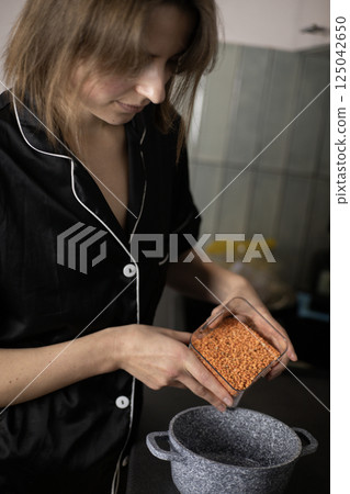 A woman pours lentils into a pot in her kitchen 125042650