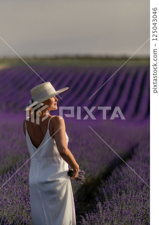 A woman in a white dress stands in a field of purple flowers 125043046