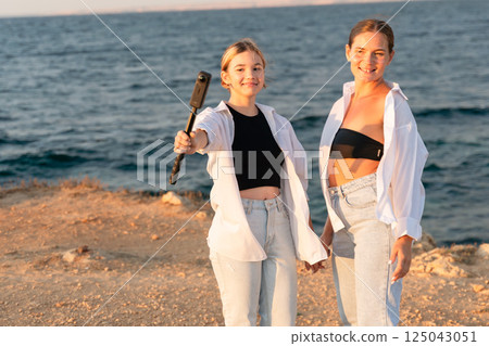 Women Beach Selfie Microphone Sunset - Two women stand on a beach with a microphone, taking a selfie during sunset. Women Beach Selfie Microphone Sunset - Two women stand on a beach with a microphone, taking a selfie during sunset. 125043051
