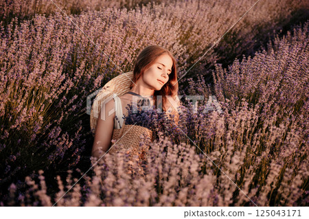 A woman is sitting in a field of lavender flowers. She is wearing a straw hat and holding a basket of flowers. The scene is peaceful and serene, with the woman enjoying the beauty of the flowers. 125043171