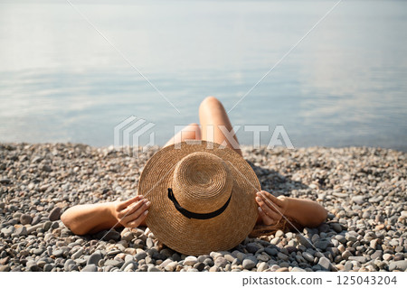 A woman is laying on the beach wearing a straw hat. She is relaxed and enjoying the sun. A woman is laying on the beach wearing a straw hat. She is relaxed and enjoying the sun. 125043204