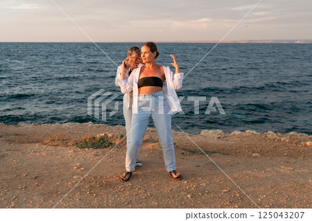 Women Friends Beach Sunset Pose - Two friends pose together by the sea at sunset. 125043207
