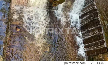 A Stunning Waterfall Cascading Beautifully Over a Stone Dam Set in Natures Embrace 125043369