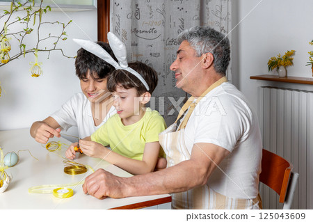 Father and sons crafting Easter decorations together at home. One boy with bunny ears and use wire for DIY ornaments. 125043609