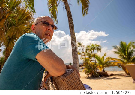 Senior man in tropical beach paradise leans on chair palm trees sand 125044273