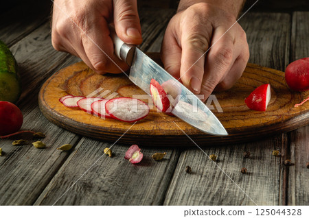 Hands skillfully slice crisp radishes on a wooden cutting board. Bright colors and textures highlight a fresh salad preparation. Sunlight streams in, enhancing the atmosphere 125044328