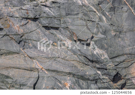 Close-up of a fractured, dark gray metamorphic rock face in natural light. Close-up of a fractured, dark gray metamorphic rock face in natural light. 125044656