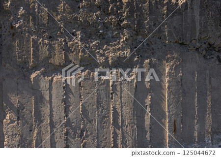 Weathered Cheap Uneven Concrete Surface with Pebbles under tangential harsh light 125044672
