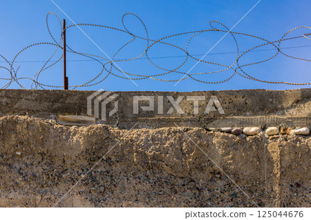Concrete wall with barbed wire against a clear blue sky. Security barrier. 125044676