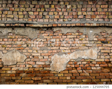Old eroded brick wall with damaged plaster leftovers Old eroded brick wall with damaged plaster leftovers 125044705