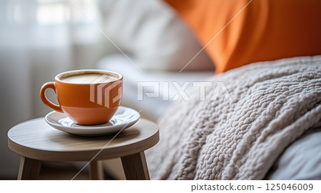 Cozy morning moment with a warm cup of coffee on a bedside table next to a comfortable bed in a softly lit room 125046009