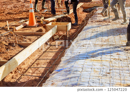 Construction crew prepares concrete foundation slab with rebar mesh for sidewalk installation workers stand around prepared formwork with wooden frames metal reinforcement mesh. Construction crew prepares concrete foundation slab with rebar mesh for sidewalk installation workers stand around prepared formwork with wooden frames metal reinforcement mesh. 125047220