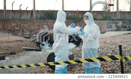 Ecologist sampling water from the river with test tube, Scientist or Biologist in a protective suit and protect mask collects sample of waste water from industrial for analyze, problem environment 125049421