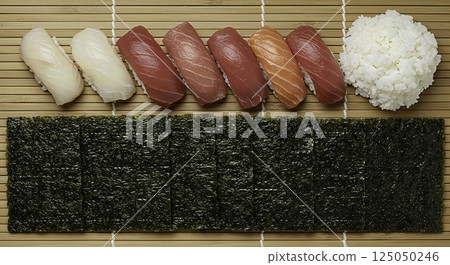 Overhead shot of sushi ingredients, nigiri with tuna, salmon, white fish, rice and nori seaweed sheets on a bamboo mat. Japanese cuisine concept. 125050246