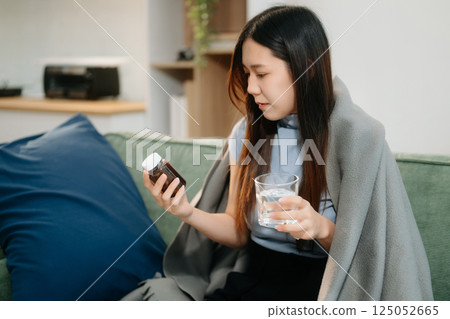 Young Asian woman suffering from flu symptoms, covered with a blanket on a sofa. Concept of illness, healthcare, 125052665
