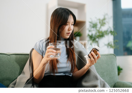 Young Asian woman suffering from flu symptoms, covered with a blanket on a sofa. Concept of illness, healthcare, 125052668