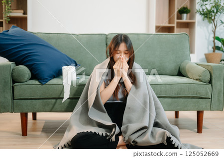Young Asian woman suffering from flu symptoms, covered with a blanket on a sofa. Concept of illness, healthcare, 125052669