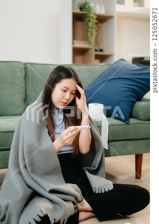 Young Asian woman suffering from flu symptoms, covered with a blanket on a sofa. Concept of illness, healthcare, 125052671
